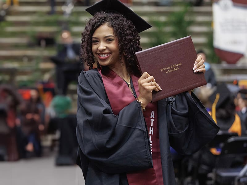 Female graduate student holding her diploma at graduation.